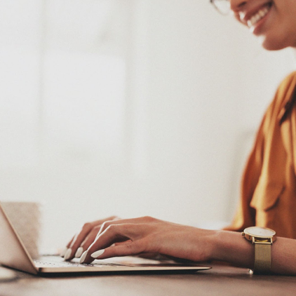 smiling person with gold shirt, manicured hands, nude watch, typing ... for example: "how to job search with a resume gap after raising kids"