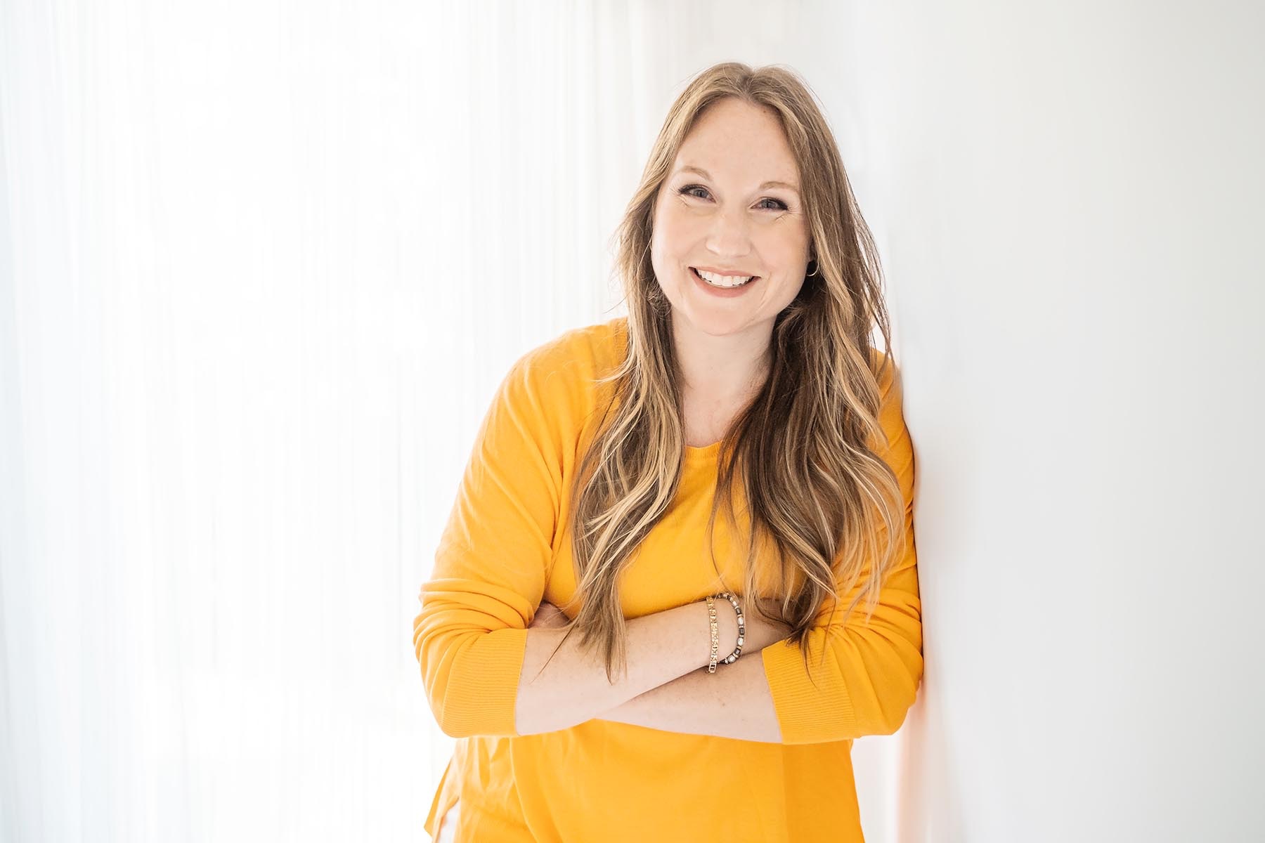 CEO and founder of Joybeforework.com Rebecca Joy, smiling, arms crossed, smiling, learning against wall
